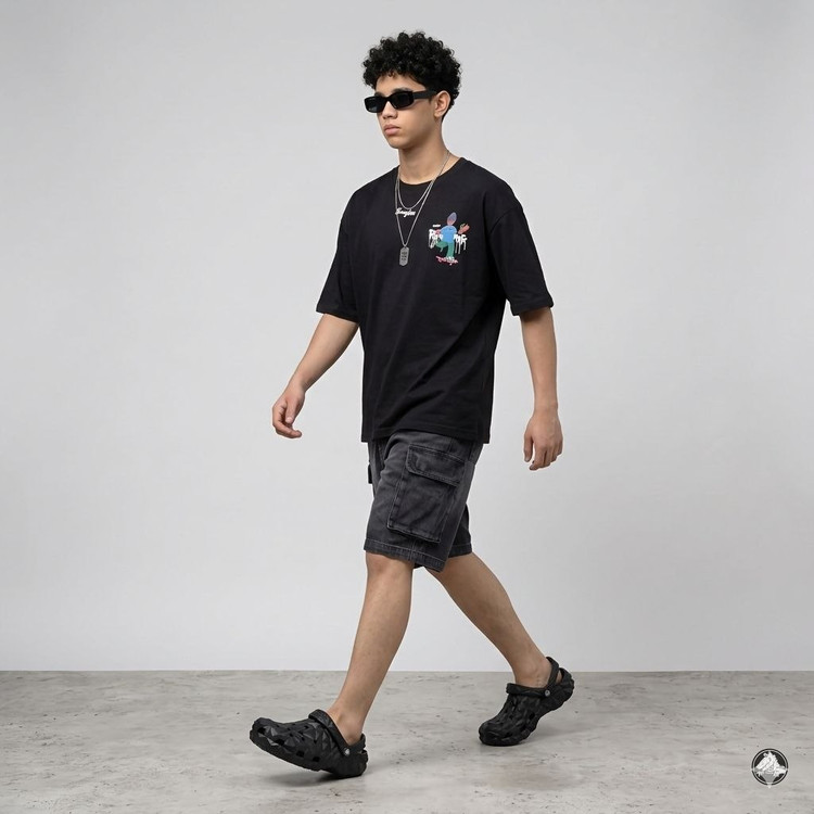 مدل مرد با استایل خیابانی شامل تیشرت مشکی گرافیکی، شلوارک کارگو و کراکس مشکی مدل ژئومتریک در فرح دخت قشم